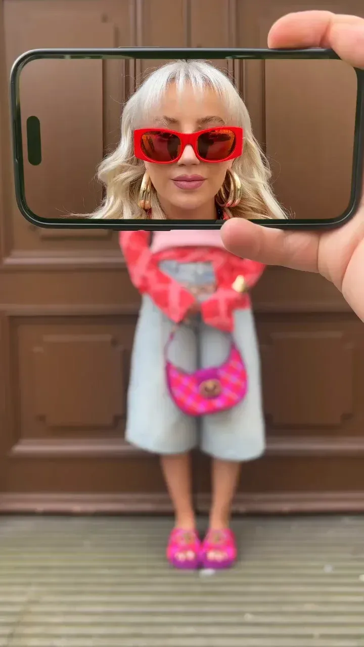 Celular erguido à frente de uma modelo, enquadrando o rosto dela na tela enquanto o corpo aparece atrás.