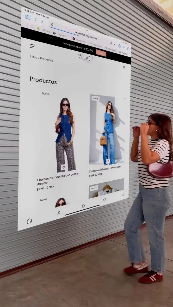 Página de produtos de um e-commerce projetada em tamanho grande sobre a fachada de uma loja, com uma cliente passando em frente.